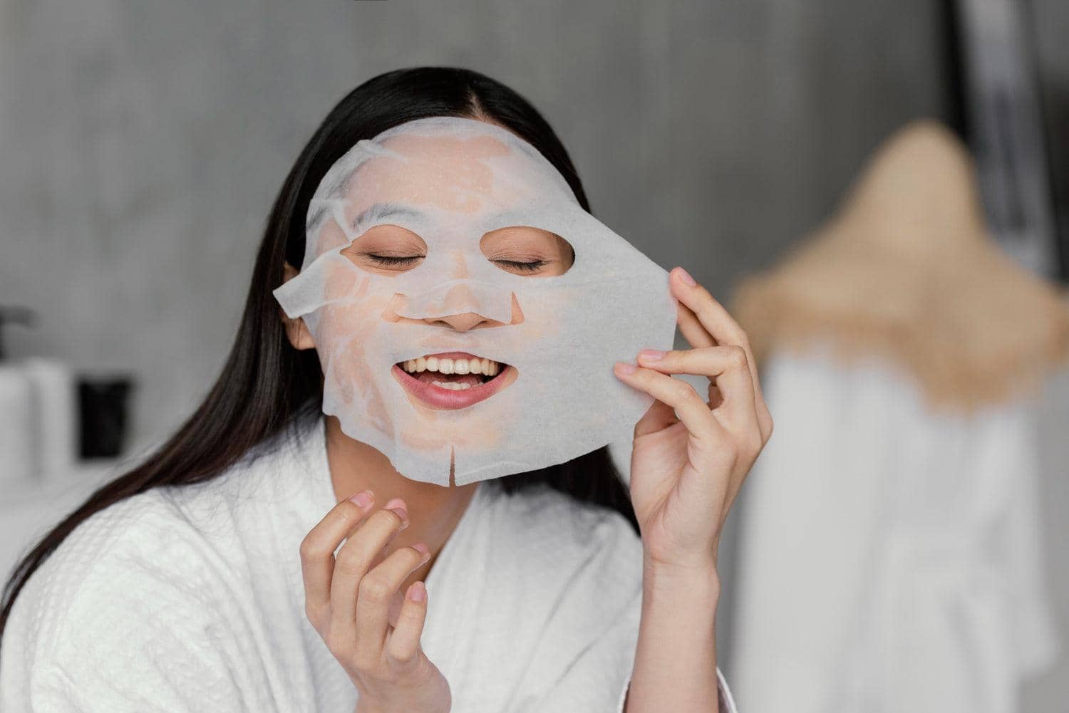 Woman applying a luxury collagen face mask while smiling in a spa-like environment