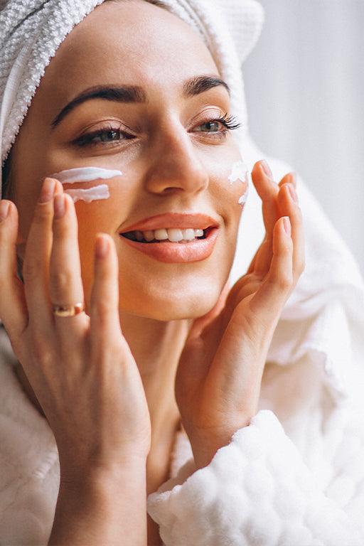 Woman applying cream on her face while smiling, showcasing summer skincare tips for radiant skin