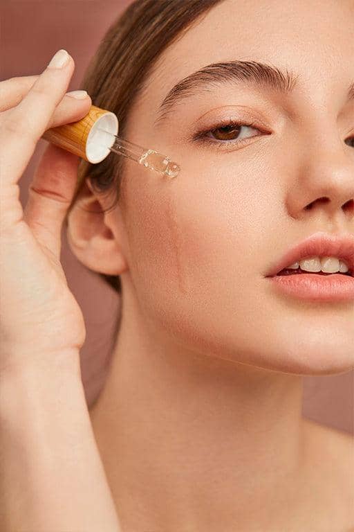 Woman applying anti-aging serums for youthful skin using a dropper on her face